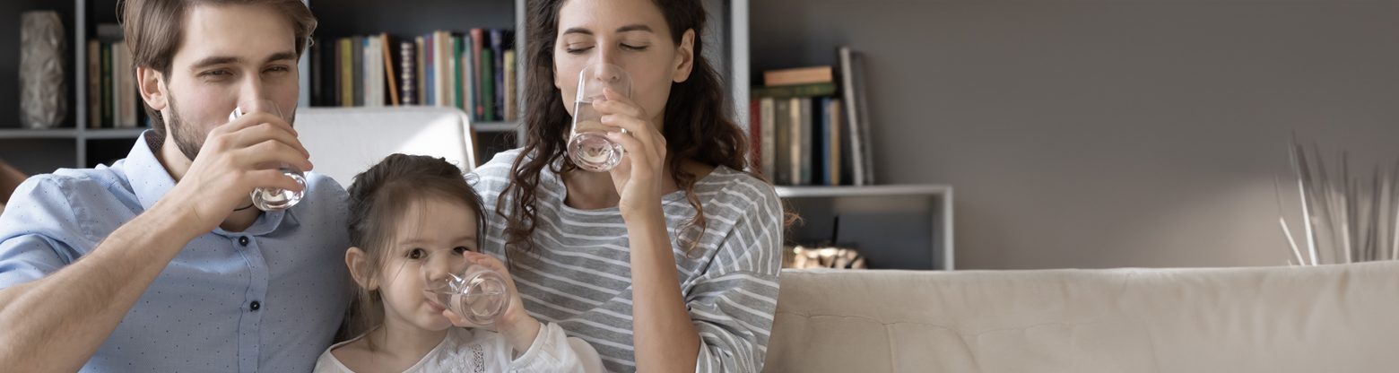 Eltern trinken mit Tochter auf dem Sofa ein Glas Wasser